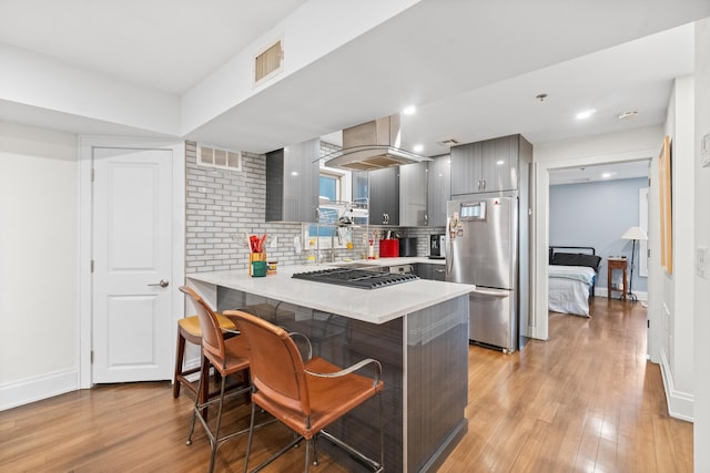 kitchen featuring appliances with stainless steel finishes, light wood-type flooring, a kitchen bar, and kitchen peninsula