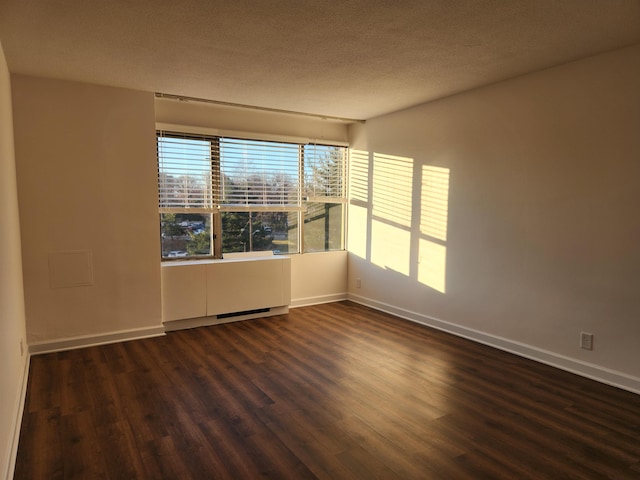 spare room featuring baseboards, dark wood-style floors, and a textured ceiling