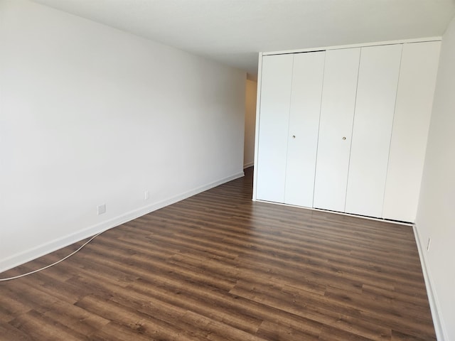 unfurnished bedroom featuring baseboards, dark wood-style floors, and a closet