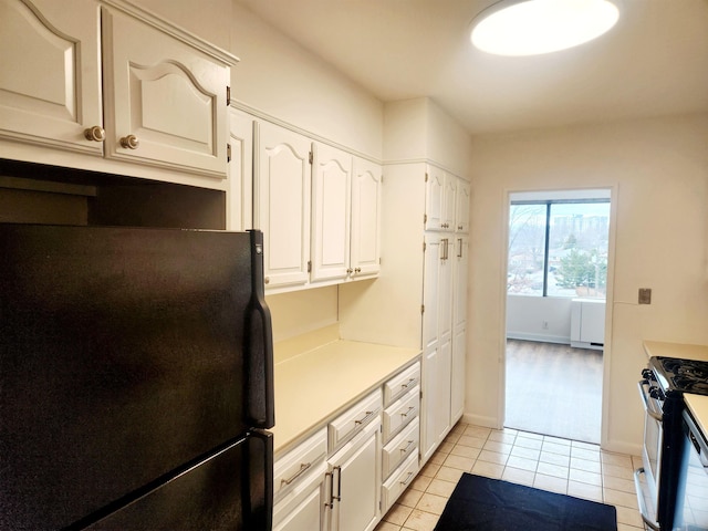 kitchen featuring stainless steel gas range, light tile patterned flooring, light countertops, white cabinetry, and freestanding refrigerator