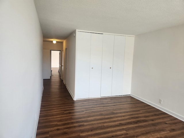 unfurnished bedroom featuring baseboards, dark wood-style floors, a textured ceiling, and a closet
