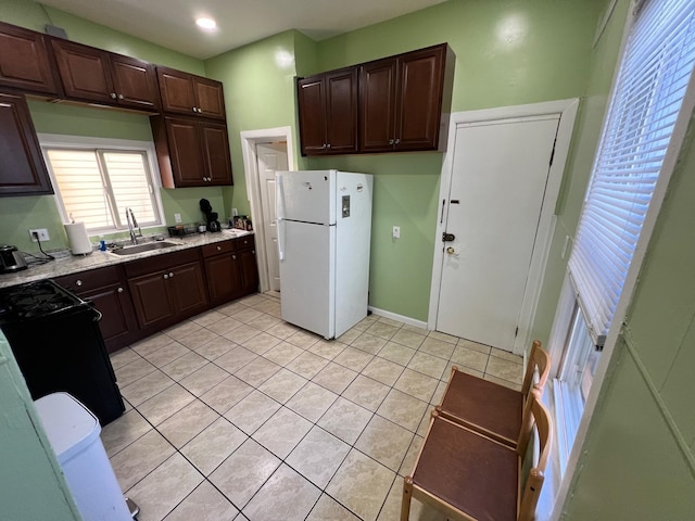 kitchen with black range, sink, light tile patterned floors, dark brown cabinets, and white fridge