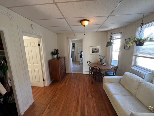 living room with a drop ceiling, wood-type flooring, and a baseboard heating unit