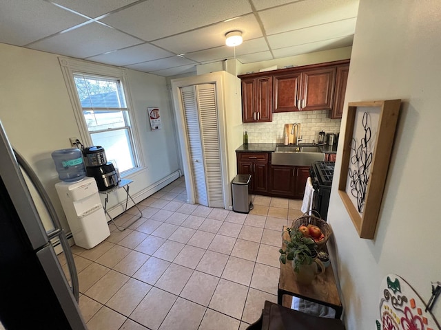 kitchen with sink, baseboard heating, backsplash, a paneled ceiling, and light tile patterned floors