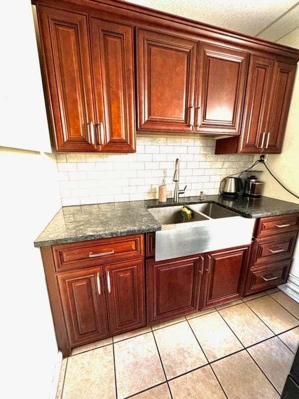 kitchen with backsplash, sink, dark stone countertops, light tile patterned floors, and a textured ceiling