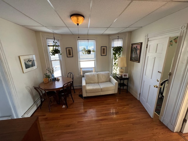 living area featuring a drop ceiling, wood-type flooring, and a baseboard heating unit