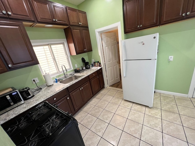 kitchen featuring dark brown cabinetry, sink, black gas range oven, white fridge, and light tile patterned flooring