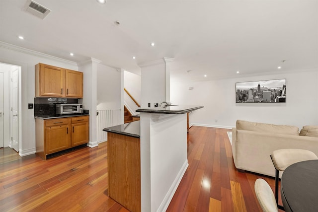 kitchen with crown molding, dark countertops, visible vents, open floor plan, and hardwood / wood-style floors