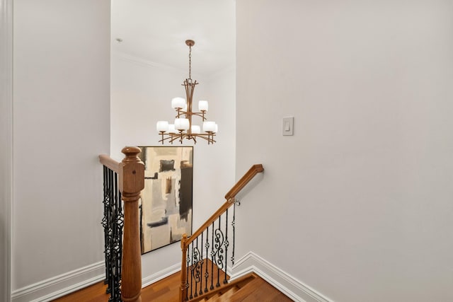 stairway with an inviting chandelier, crown molding, baseboards, and wood finished floors