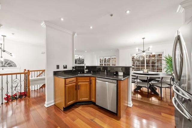 kitchen featuring light wood-style flooring, stainless steel appliances, a sink, brown cabinets, and an inviting chandelier