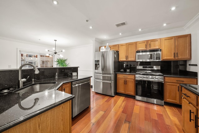 kitchen featuring light wood-style flooring, appliances with stainless steel finishes, brown cabinets, crown molding, and a sink