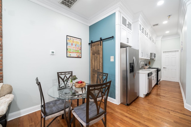 kitchen featuring crown molding, a barn door, white cabinets, and appliances with stainless steel finishes