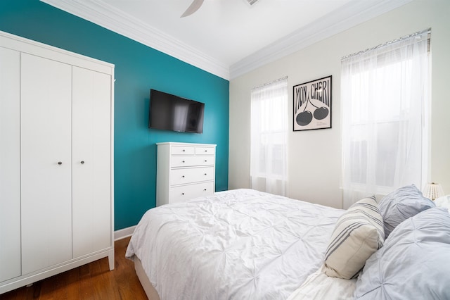 bedroom featuring multiple windows, dark wood-type flooring, ornamental molding, and a closet