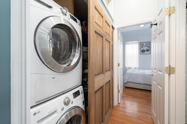 laundry room with light hardwood / wood-style floors and stacked washing maching and dryer