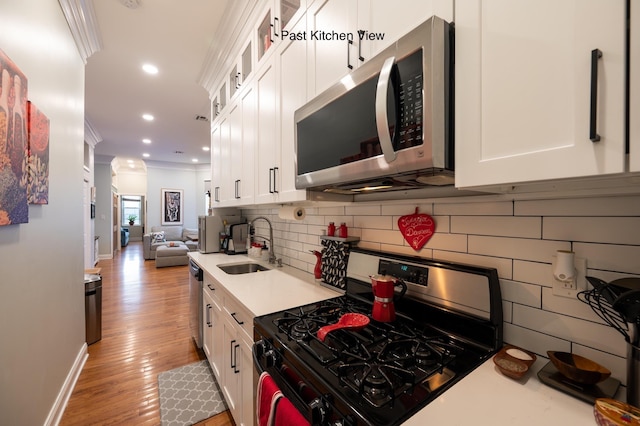 kitchen with sink, white cabinetry, ornamental molding, stainless steel appliances, and decorative backsplash