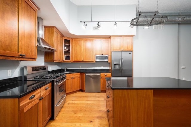 kitchen with light wood finished floors, wall chimney exhaust hood, dark countertops, and appliances with stainless steel finishes