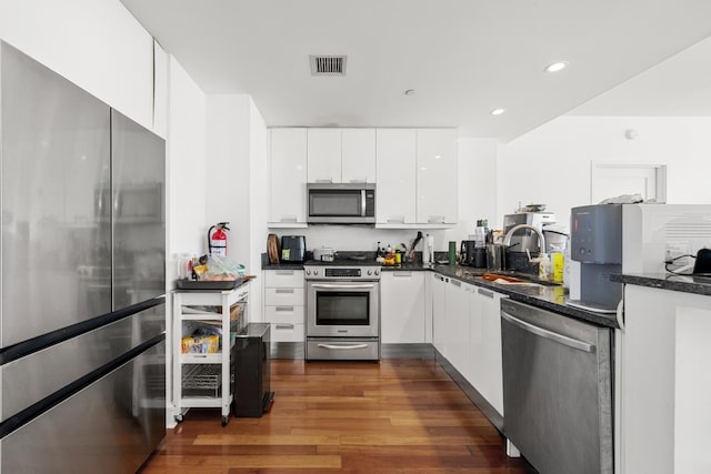 kitchen with appliances with stainless steel finishes, dark stone counters, dark wood-type flooring, sink, and white cabinets