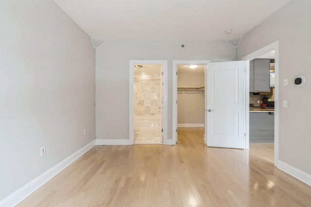 unfurnished bedroom with light hardwood / wood-style flooring, ensuite bath, a walk in closet, and a closet