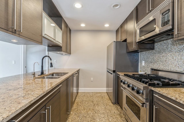 kitchen featuring sink, backsplash, stainless steel appliances, light stone countertops, and dark brown cabinets