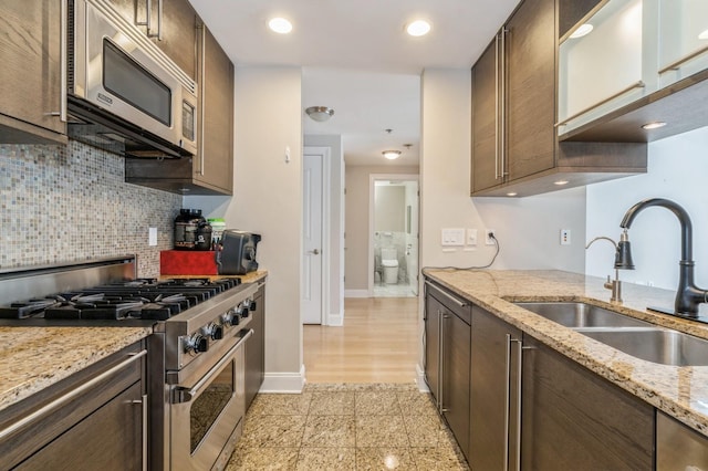 kitchen with sink, tasteful backsplash, dark brown cabinets, stainless steel appliances, and light stone countertops