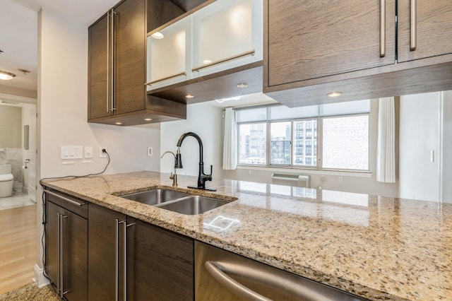 kitchen with dark brown cabinetry, light stone countertops, sink, and light wood-type flooring