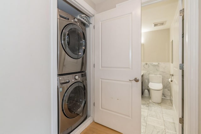 clothes washing area featuring stacked washer / drying machine and tile walls