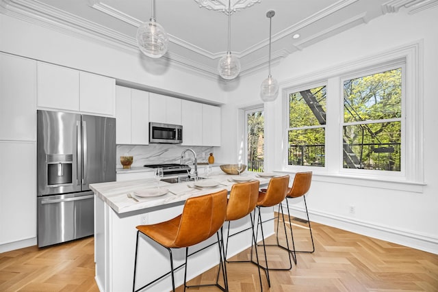 kitchen featuring white cabinets, hanging light fixtures, stainless steel appliances, light parquet flooring, and a center island with sink