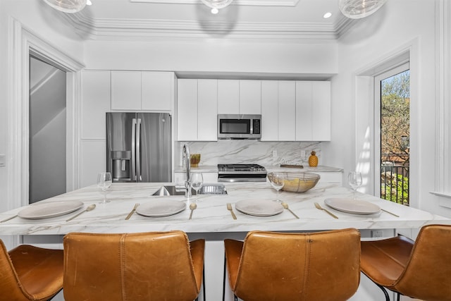 kitchen with a kitchen bar, backsplash, white cabinets, and appliances with stainless steel finishes