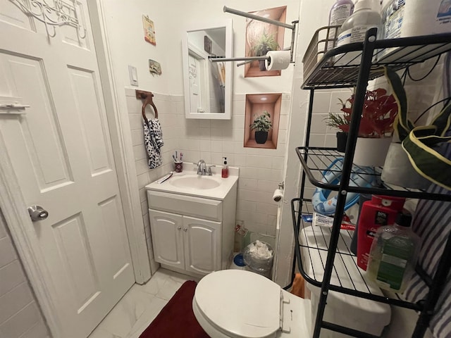 bathroom with tile walls, marble finish floor, vanity, and toilet