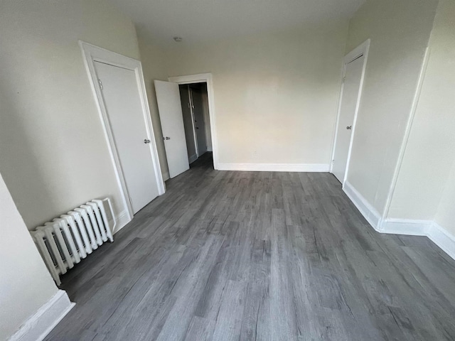 empty room featuring dark wood finished floors, radiator heating unit, and baseboards