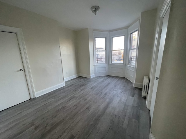 empty room with dark wood finished floors, radiator heating unit, and baseboards