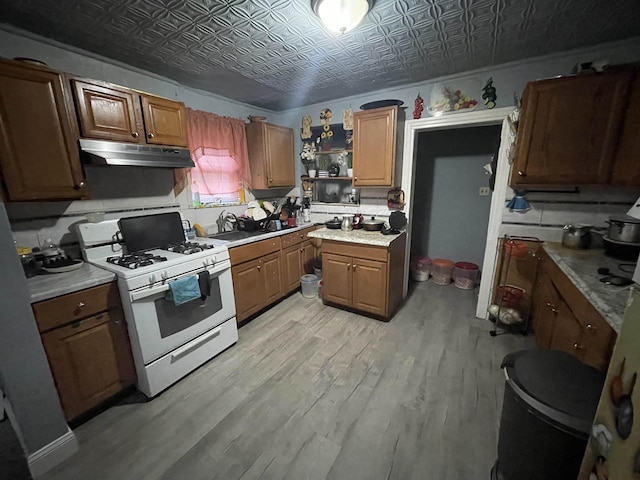 kitchen featuring under cabinet range hood, white range with gas stovetop, an ornate ceiling, and light wood finished floors