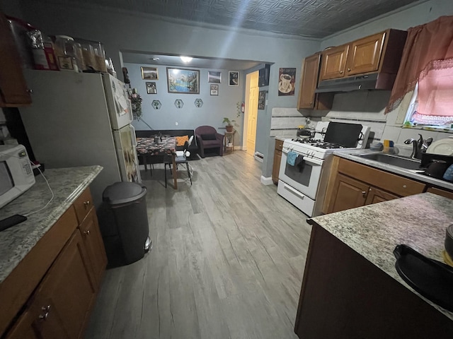 kitchen with a sink, under cabinet range hood, an ornate ceiling, white appliances, and light wood finished floors