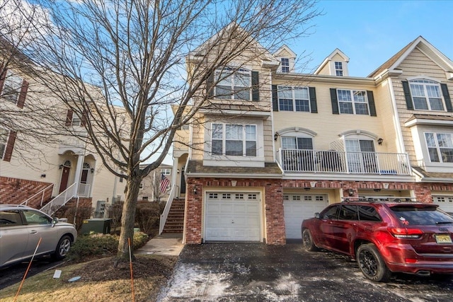 view of property featuring brick siding, driveway, an attached garage, and stairs