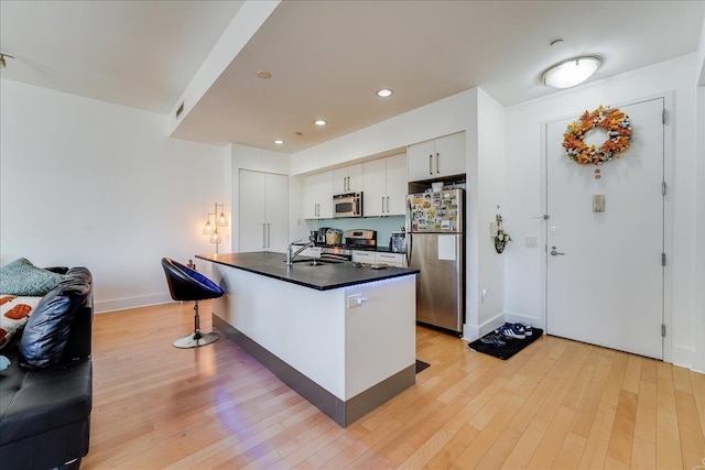 kitchen featuring appliances with stainless steel finishes, sink, light hardwood / wood-style flooring, white cabinetry, and a breakfast bar area