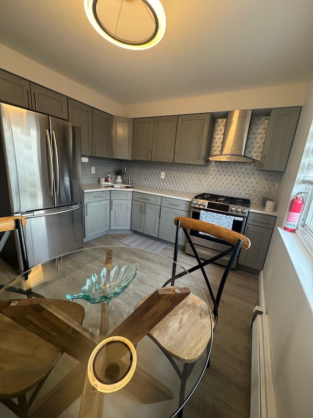 kitchen with tasteful backsplash, appliances with stainless steel finishes, gray cabinets, light countertops, and wall chimney range hood