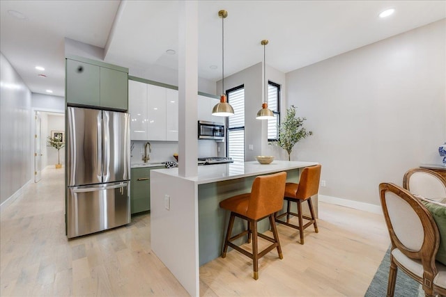 kitchen with a center island, a breakfast bar area, decorative light fixtures, light hardwood / wood-style floors, and stainless steel appliances