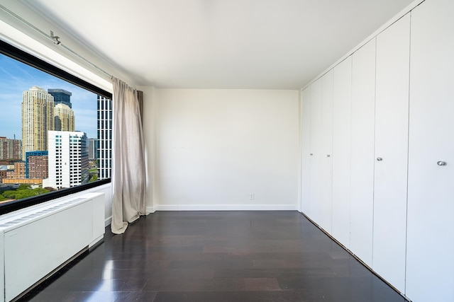 135 Montgomery St Unit 21H, Jersey City, NJ 07302 - unfurnished bedroom featuring dark wood-style flooring, baseboards, a closet, and a view of skyline