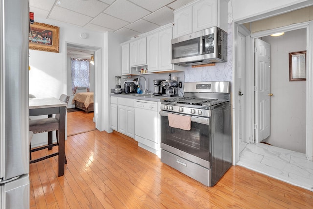 9 E 15th St, Bayonne, NJ 07002 - kitchen featuring appliances with stainless steel finishes, white cabinets, light wood finished floors, light countertops, and a paneled ceiling