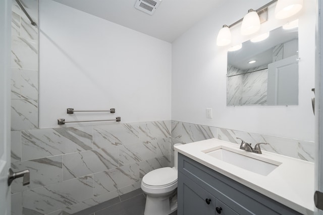 full bathroom featuring toilet, vanity, visible vents, tile walls, and walk in shower