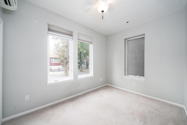 carpeted spare room featuring an AC wall unit, ceiling fan, and baseboards