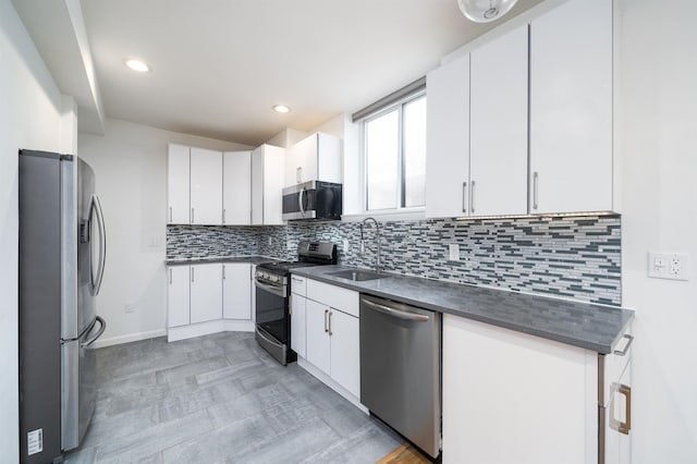 kitchen featuring stainless steel appliances, a sink, white cabinets, backsplash, and dark countertops