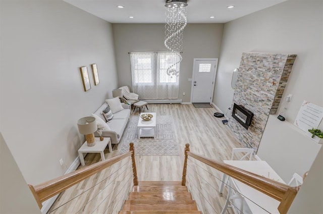 living room featuring an inviting chandelier, a stone fireplace, a high ceiling, and light wood-type flooring