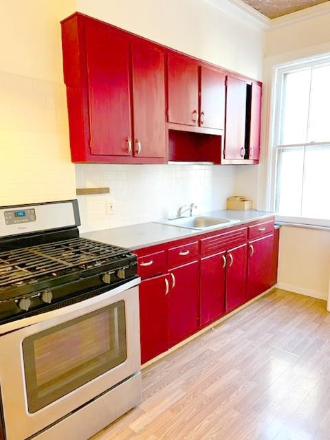 kitchen featuring sink, tasteful backsplash, ornamental molding, stainless steel gas range oven, and light wood-type flooring