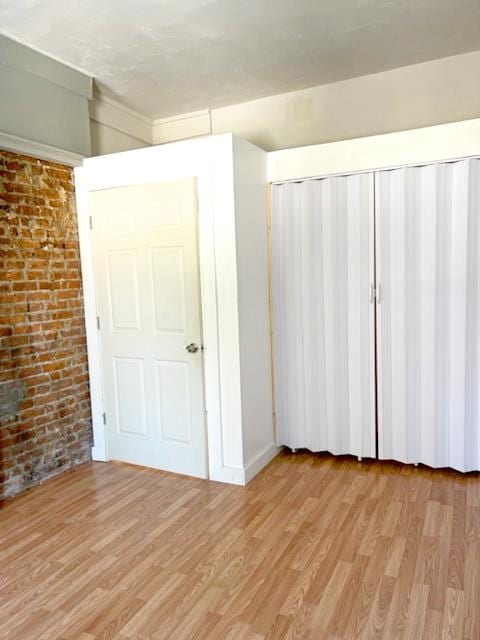 unfurnished bedroom with light hardwood / wood-style flooring and brick wall