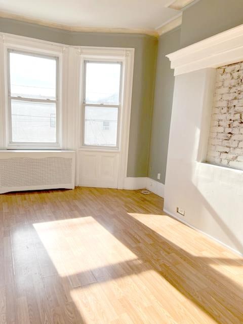 empty room featuring radiator, wood-type flooring, and crown molding