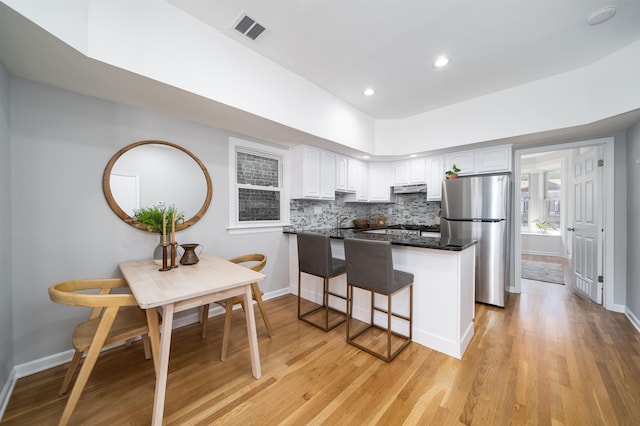 kitchen with stainless steel refrigerator, kitchen peninsula, a breakfast bar area, light hardwood / wood-style flooring, and white cabinets