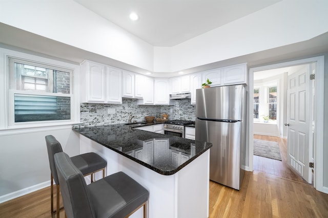 kitchen with stainless steel appliances, dark stone counters, a breakfast bar area, white cabinets, and decorative backsplash