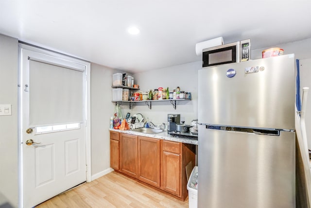 kitchen with light stone counters, sink, stainless steel appliances, and light wood-type flooring