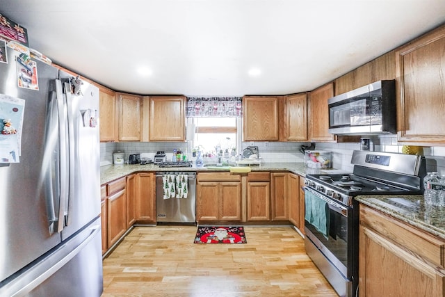 kitchen with decorative backsplash, light wood-type flooring, stainless steel appliances, sink, and stone counters